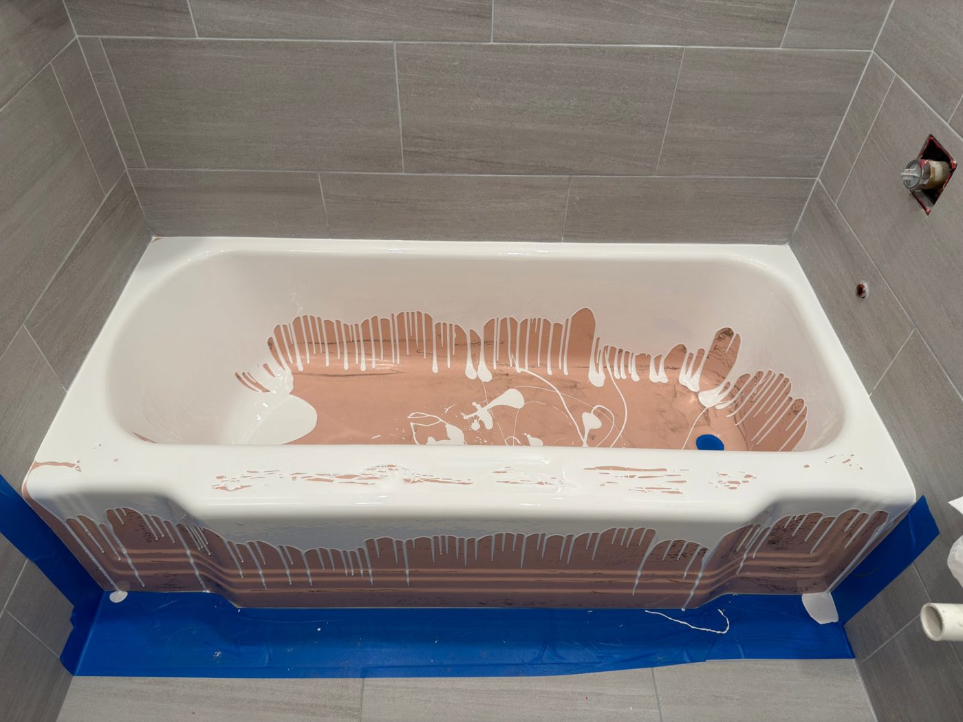 White coating being poured over a pink cast iron bathtub during refinishing